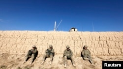 U.S. Army soldiers sit behind a wall as others search for explosives after an improvised-explosive-device blast damaged an armored vehicle during a road-clearance patrol in Logar Province in eastern Afghanistan.