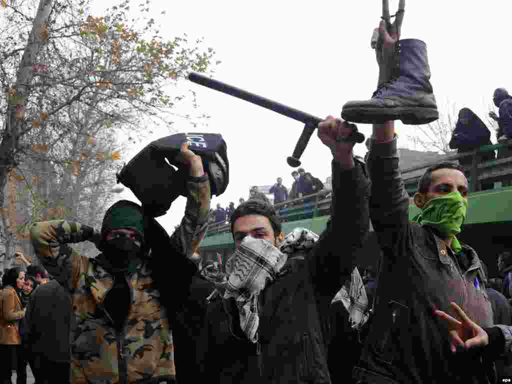 Protesters hold a boot, baton, and bulletproof vest apparently taken from a Tehrani police officer. (AFP)